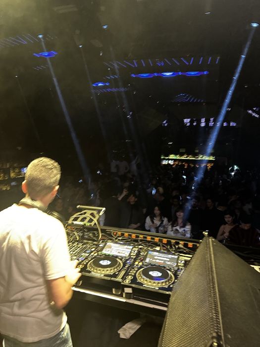 Behind the CDJs facing the crowd